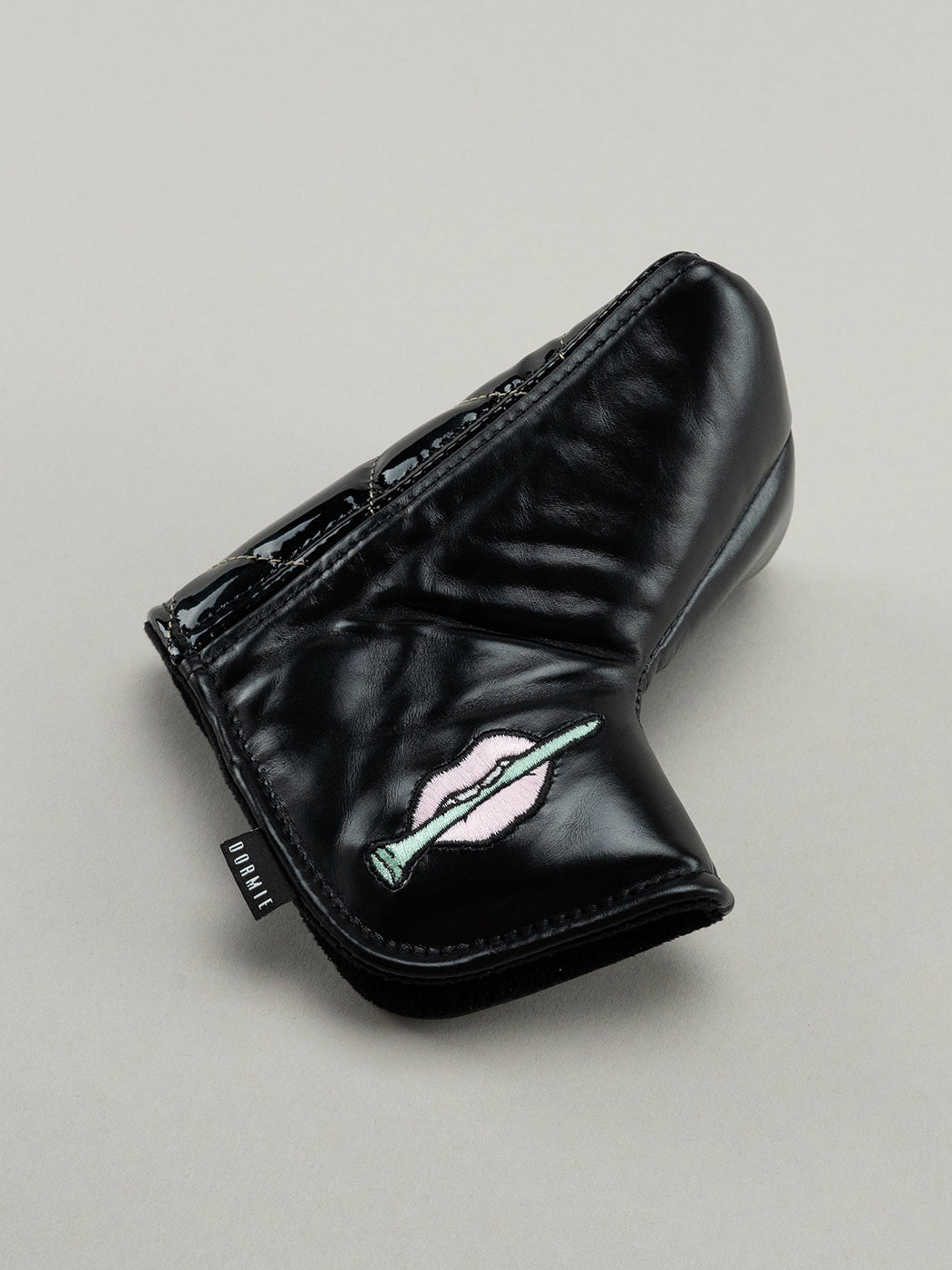 Black quilted leather golf headcover with small icon of embroidered lips clutching a golf tee.